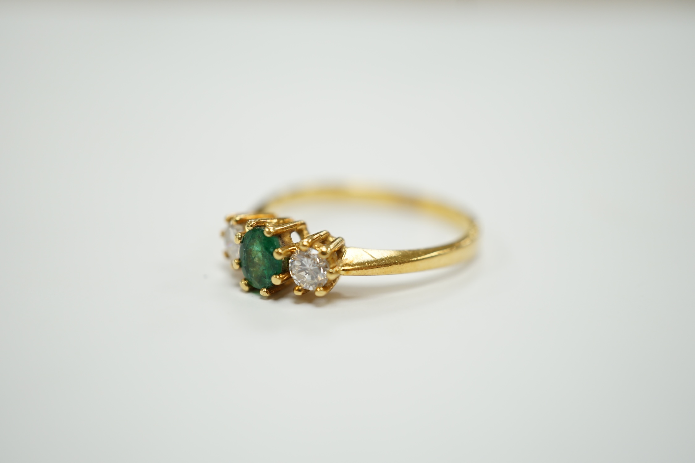 A modern 18ct gold, emerald and diamond set three stone ring, size P, gross weight 3.2 grams.